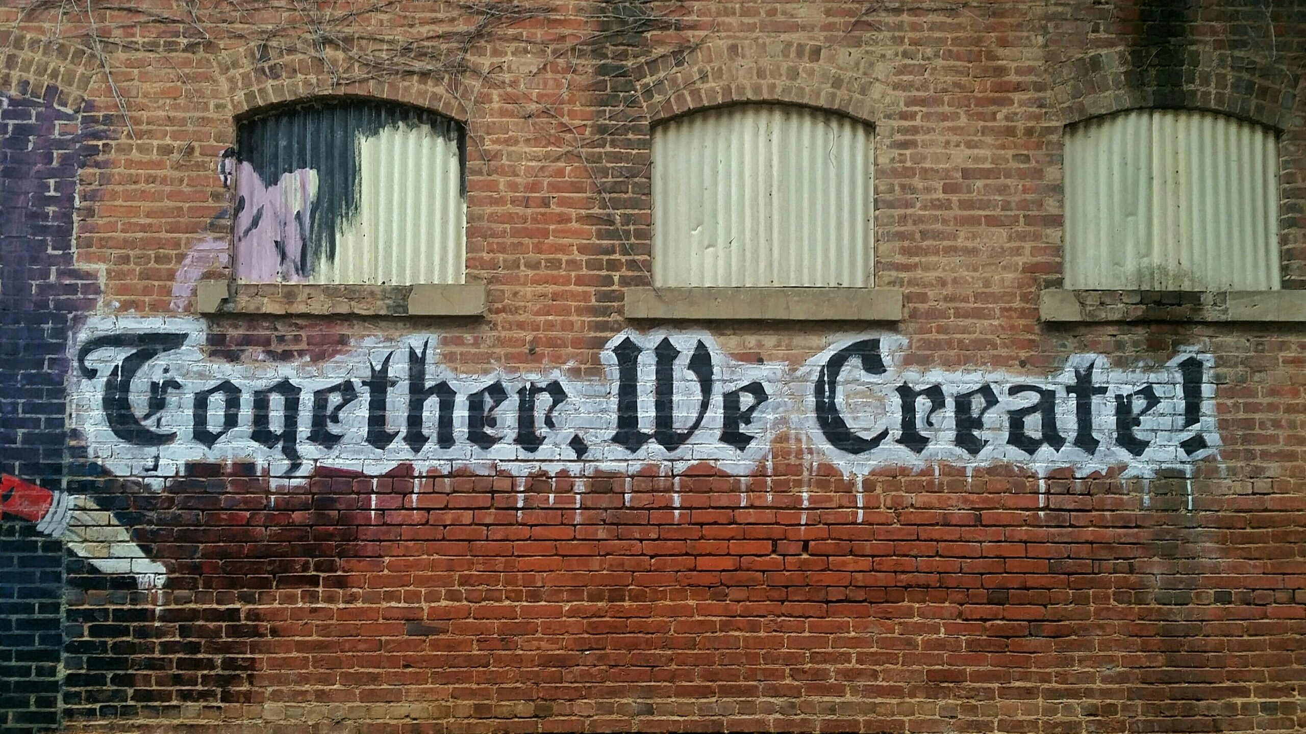Graffiti Kunst auf einem Haus, abgebildet ist ein Schriftzug "Together we create" mit einem Pinsel mit Farbe